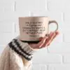 A person holding a coffee mug with the words " she is clothes in progress ".
